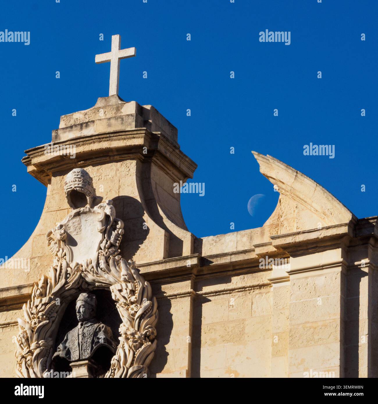 Statue eines Mannes mit Kreuz und Mond, sichtbar am Himmel über dem Gebäude in Valletta, Malta, mit einem klaren blauen Himmel. Stockfoto