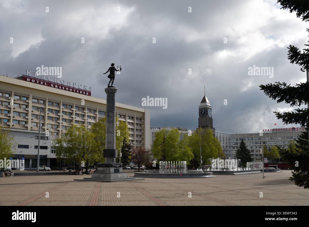 Krasnojarsk, Russland - 22. Mai 2026: Theaterplatz. Der Uhrenturm über dem Verwaltungsgebäude der Stadt, der Brunnen, die Statue des Apollon und die Stockfoto