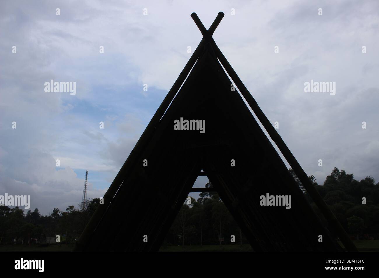 Dunkle Silhouette eines Tipi-ähnlichen Bambus-Schutzhauses vor bewölktem Himmel, Außenstruktur, natürliche Konstruktion, einzigartige Form. Stockfoto