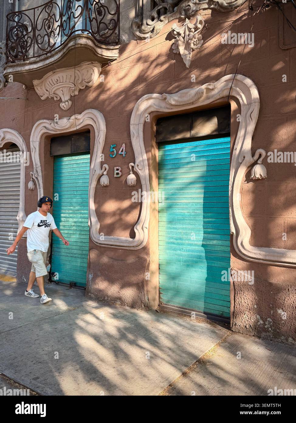 Ein Fußgänger passiert eine verzierte Fassade aus dem frühen 20. Jahrhundert mit Jugendstil-Details und türkisfarbenen Rollläden in Roma Norte, Mexiko-Stadt Stockfoto