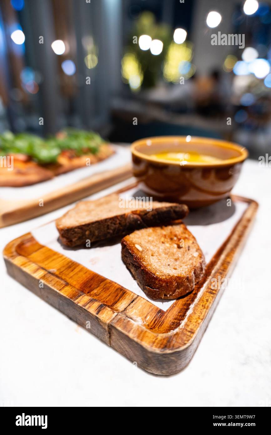 Warme geröstete Brotscheiben und eine Schüssel Suppe auf rustikalem Holzbrett im gemütlichen Restaurant mit Stockfoto