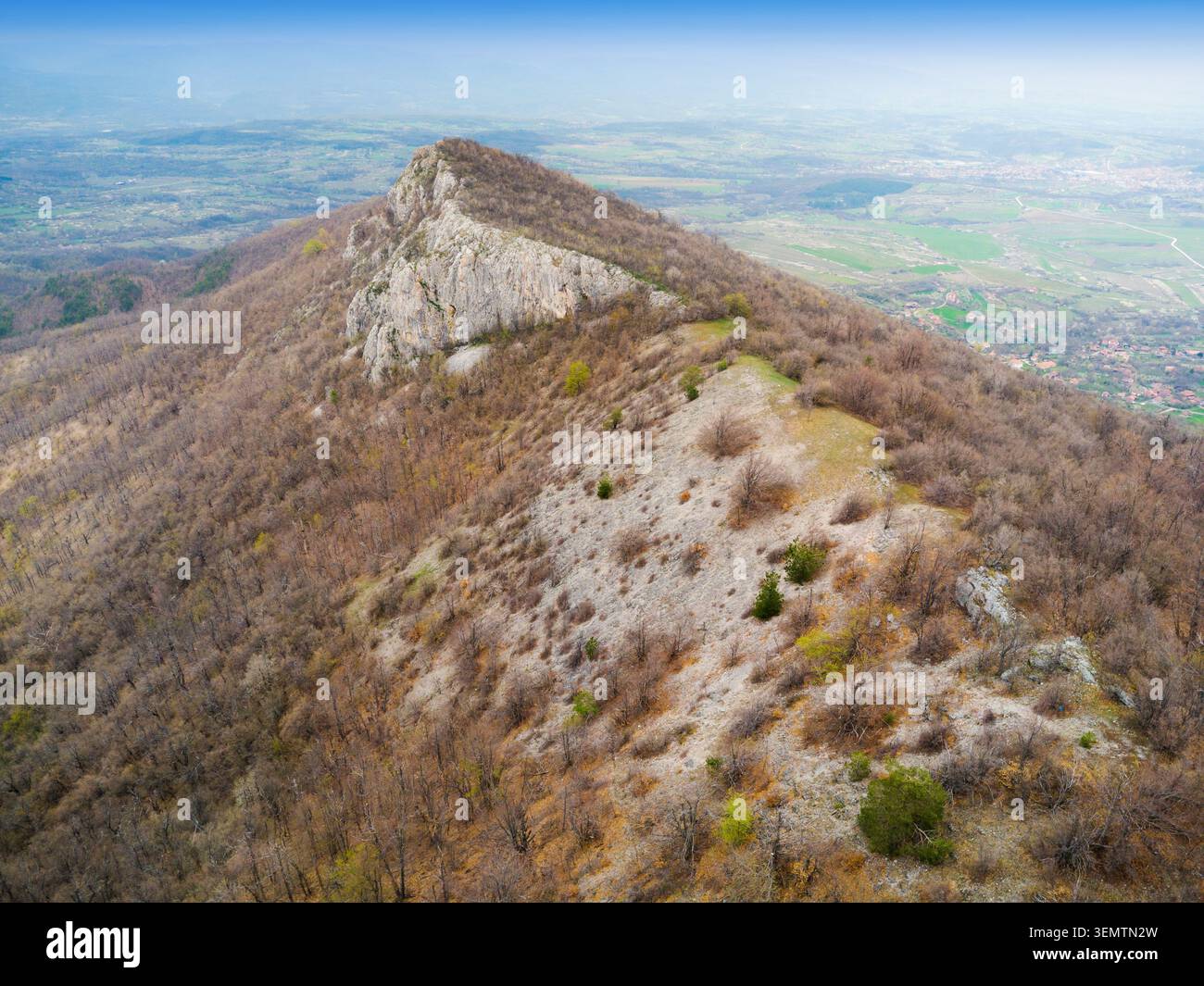 Aus der Vogelperspektive entdecken Sie einen zerklüfteten Bergrücken, der einen bewaldeten Hang von einer felsigen Klippe trennt, mit einem weiten Tal in der Ferne Stockfoto