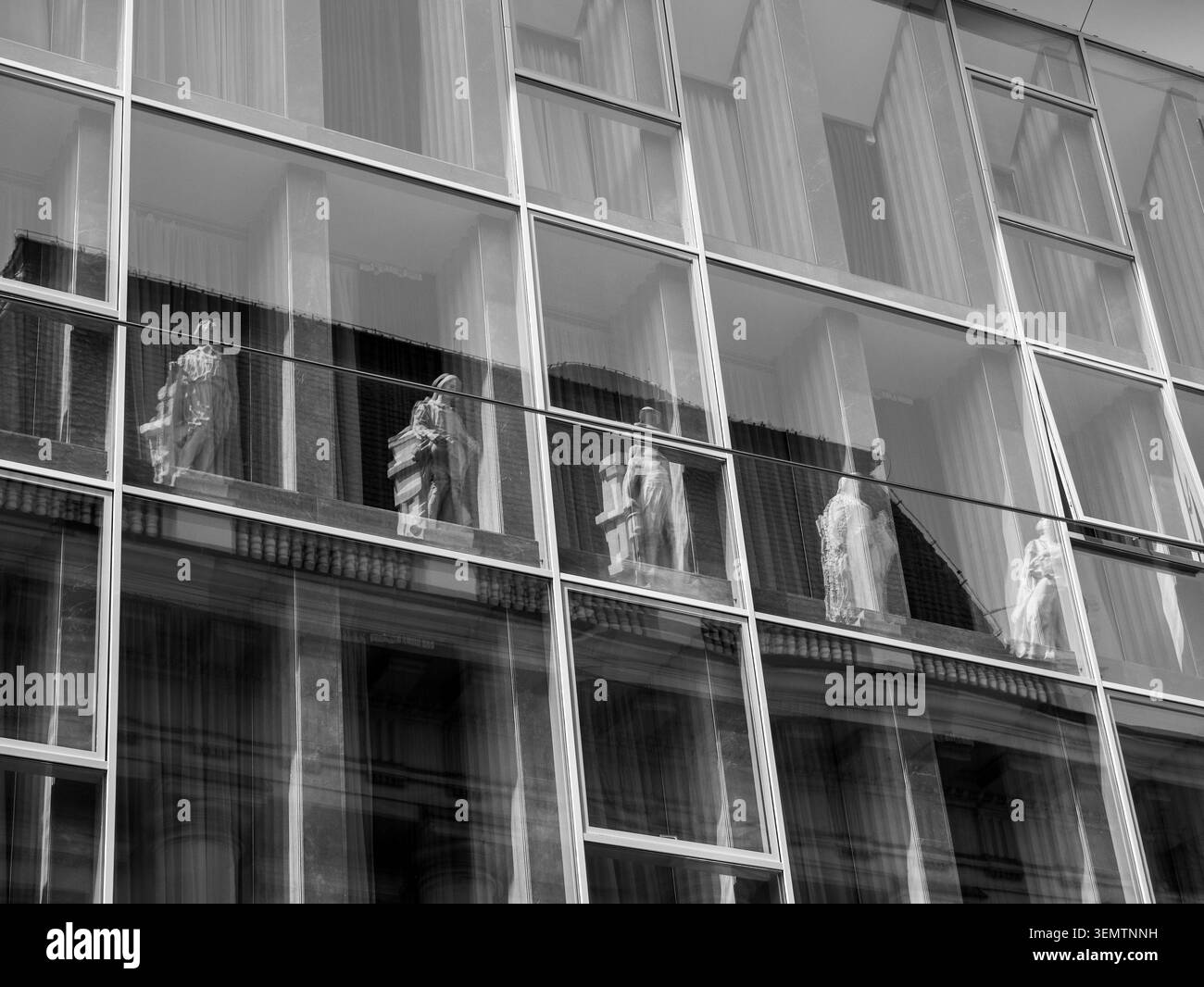 Die Reflexionen klassischer Steinstatuen aus einem historischen neoklassizistischen Gebäude sind in der deckenhohen Glasvorhangfassade eines modernen Offik festgehalten Stockfoto
