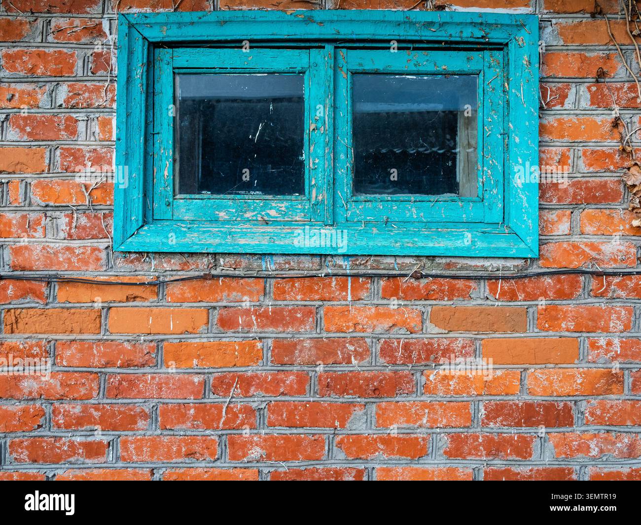 Die gemauerte Ziegelwand der alten Scheune mit einem kleinen abblätternden Fensterrahmen, der im Dorf grün gestrichen wurde Stockfoto