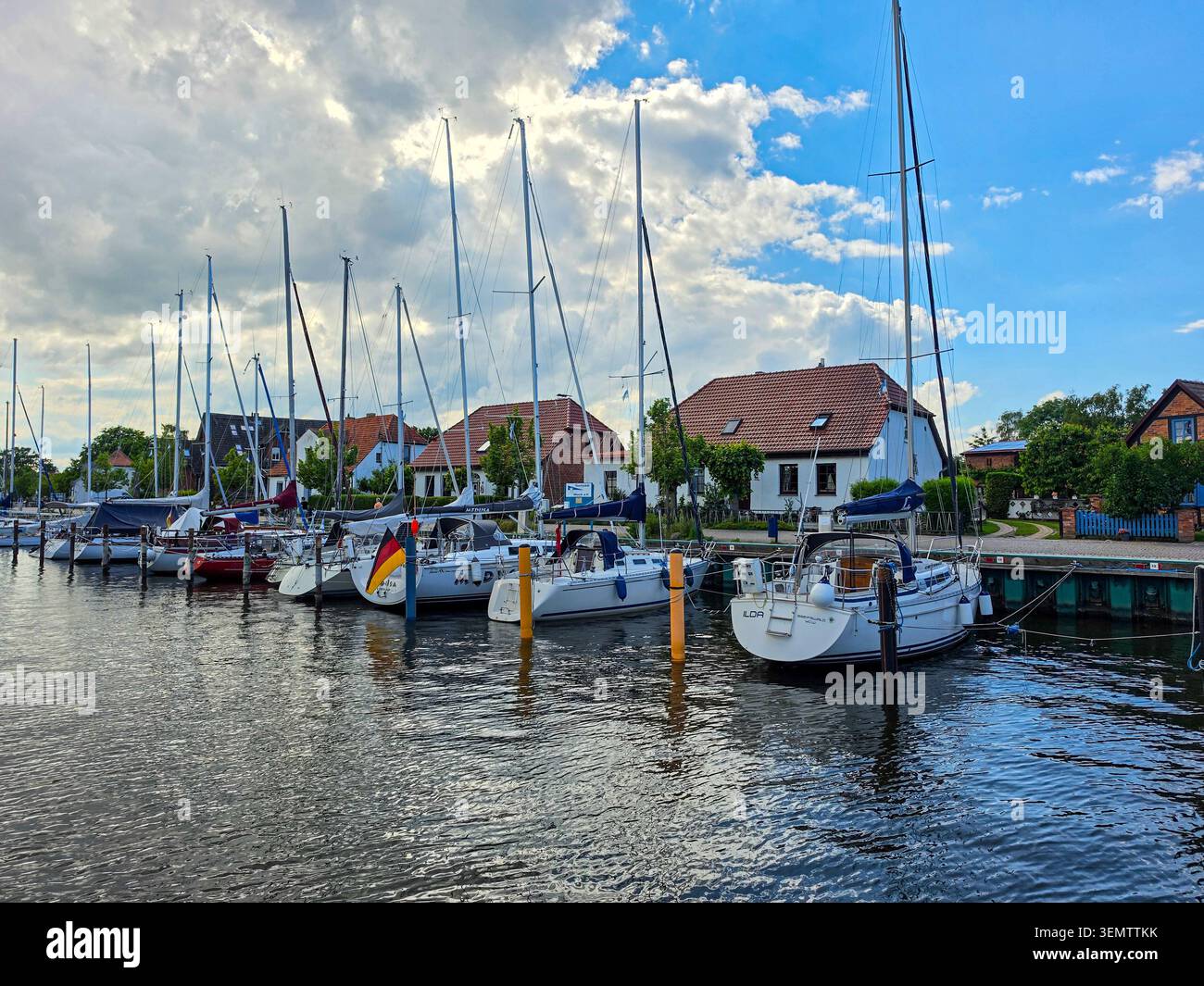 Segelboote, die an einem sonnigen Tag in einem malerischen Yachthafen mit traditionellen Häusern am Wasser vor Anker liegen Stockfoto