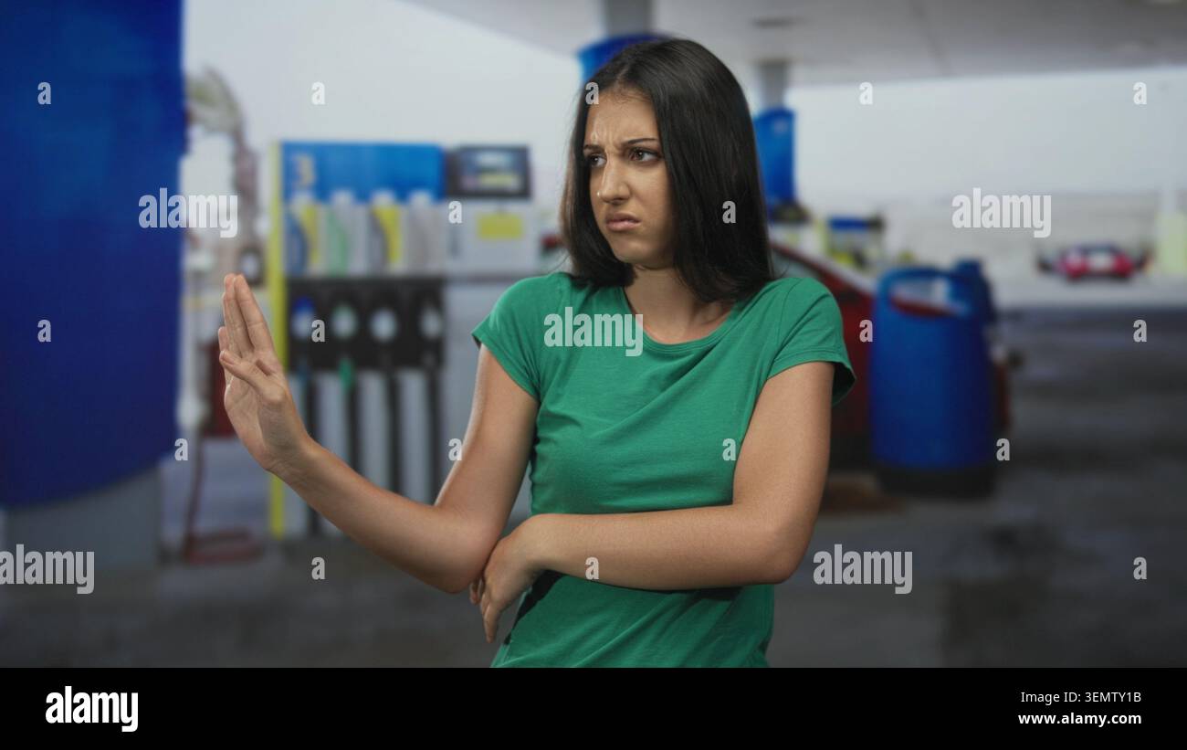 Die Frau drückt die Hände weg und dreht den Kopf mit einem ekelhaften Blick in der Nähe einer Kraftstoffpumpe in einem Tankstellengebäude; Ekel-Weigerung-Grenze. Stockfoto