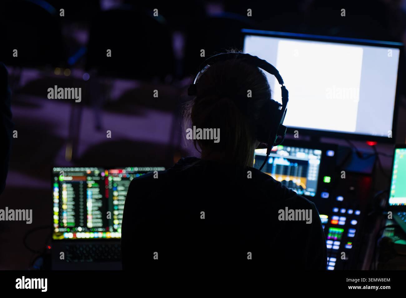 Ein Audio-Video-Spezialist überwacht die Produktionssoftware für mehrere Bildschirme auf einem interaktiven Display-Terminal in einer Technikkontrollstation Stockfoto