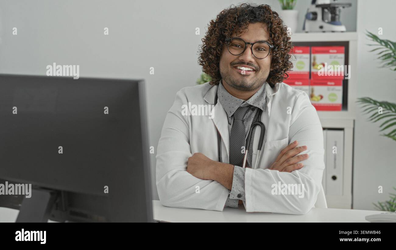 Mann Doktor mit Stethoskop, Arme überkreuzt am Klinikpult, lächelt in die Kamera, Mitgefühl Selbstvertrauen. Stockfoto