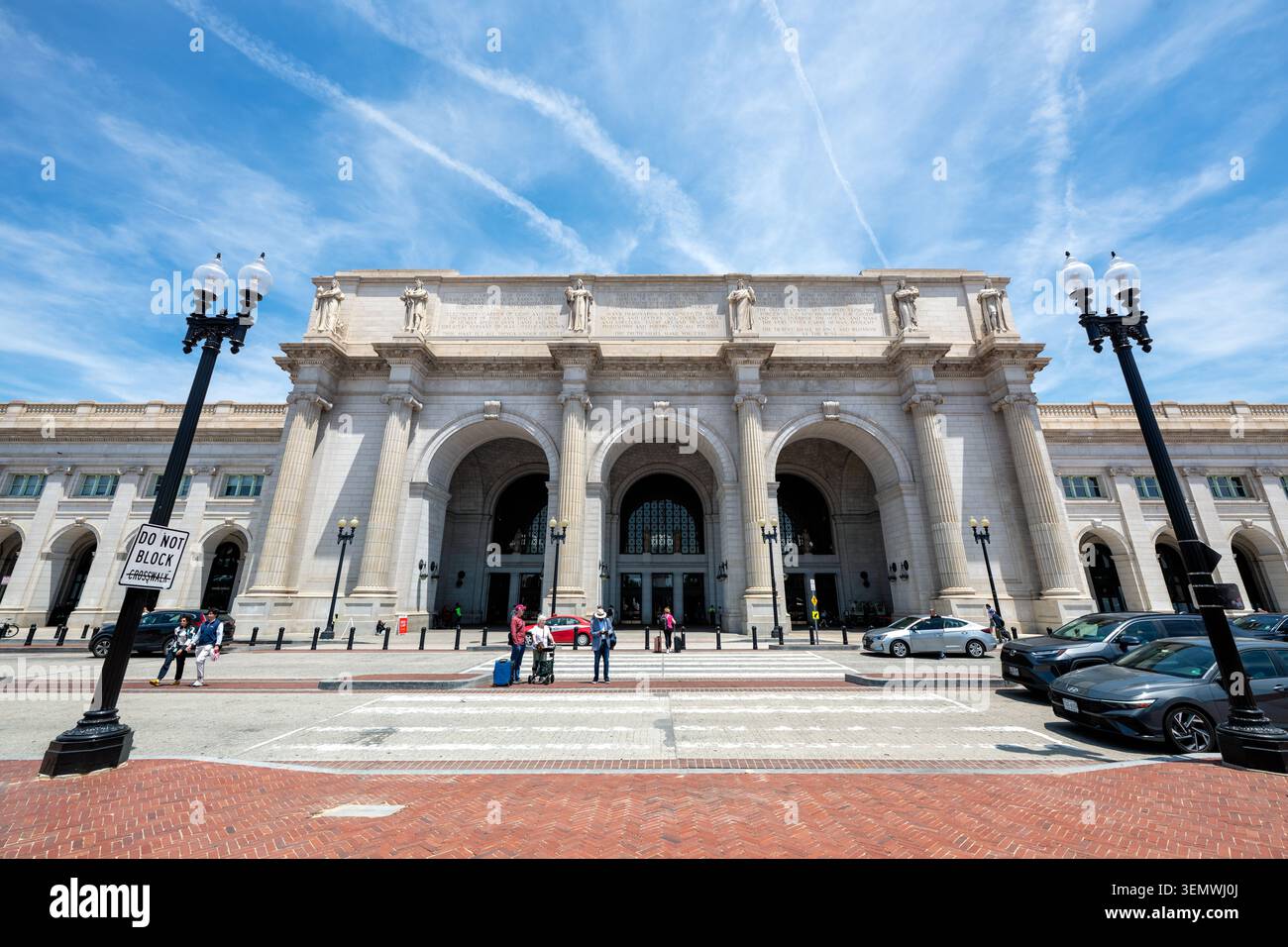 Inschriften an der Fassade der Union Station Washington DC | WASHINGTON D.C., Vereinigte Staaten — Fußgänger und Reisende überqueren die Massachusetts Avenue NE unter dem dreifachen Bogen des zentralen Pavillons der Union Station. Der Harvard-Präsident Charles W. Eliot verfasste die Inschriften, die in den Granitfries über dem Portal eingemeißelt sind, und erklärt Louis Saint-Gaudens‘ sechs allegorische Figuren zu den Themen Feuer, Elektrizität, Freiheit und Mechanik. Stockfoto