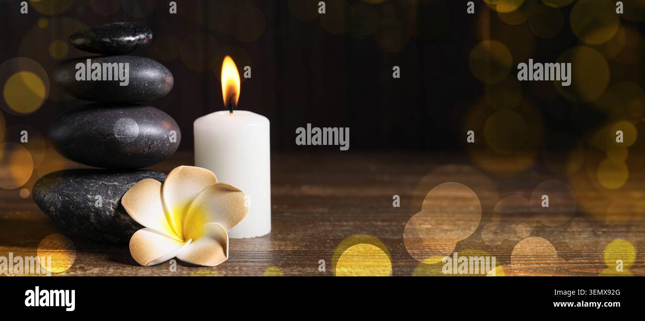 Spa Wellness mit Zen-Steinen, beleuchteter Kerze und Frangipani-Blume auf dunklem Holzhintergrund mit Bokeh Stockfoto