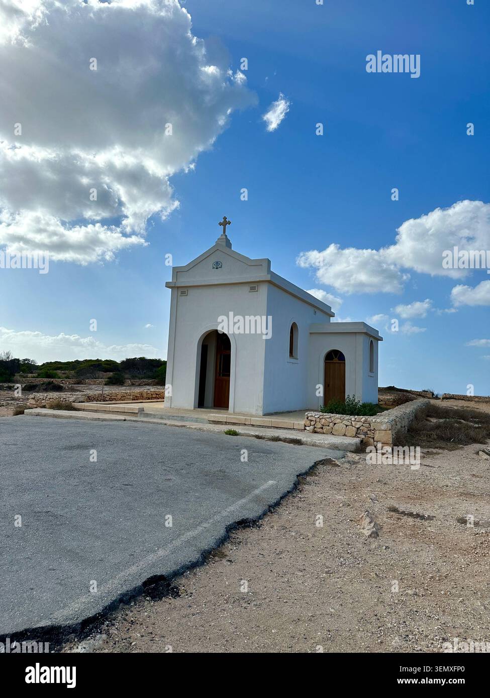 Eine kleine weiße Kapelle steht vor einem blauen Himmel auf einem trockenen mediterranen Hügel. - Smartphone-aufgenommenes Stockfoto