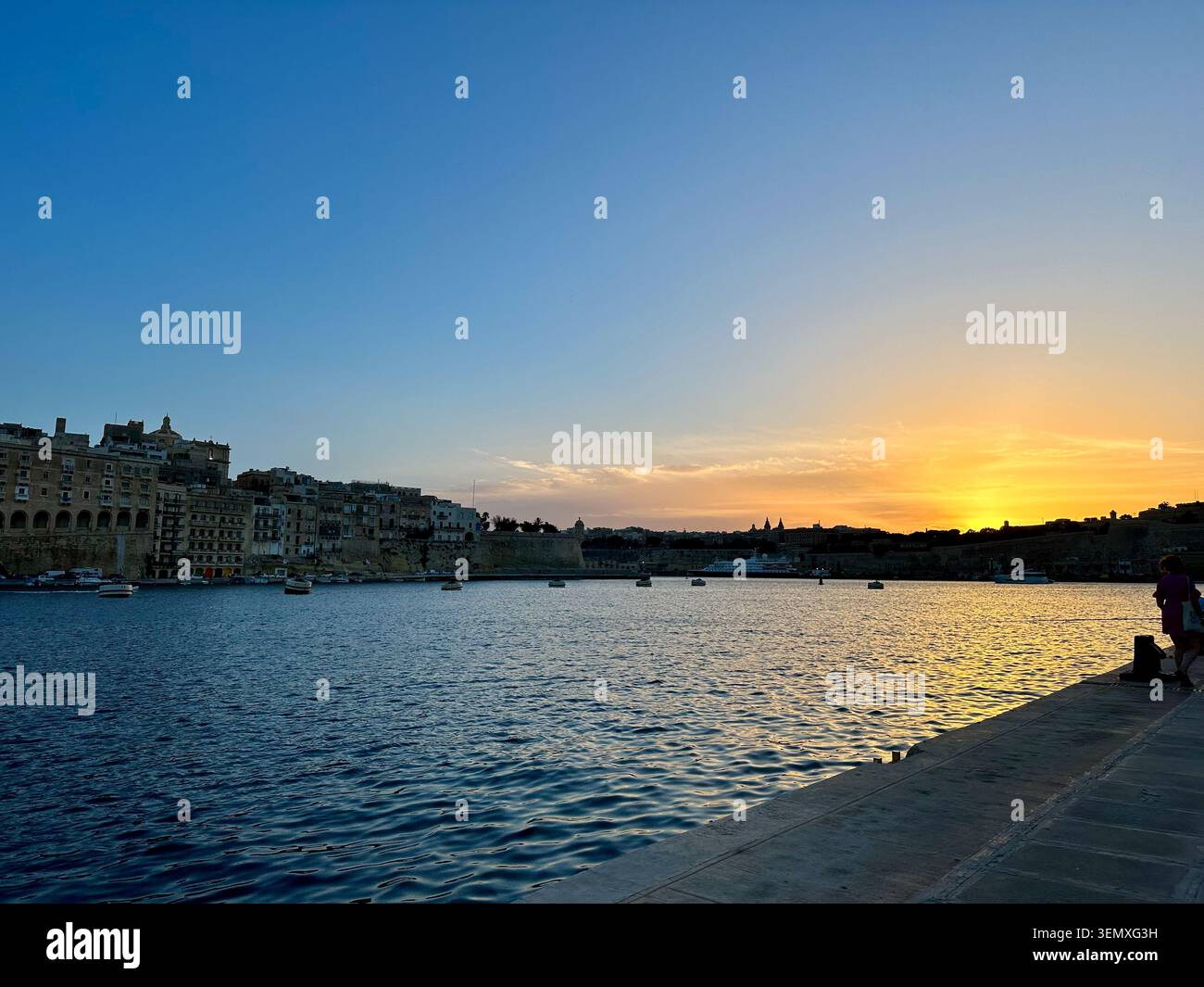 Sonnenuntergang über Maltas historischem Hafenufer mit goldenem Himmel. - Smartphone-aufgenommenes Stockfoto