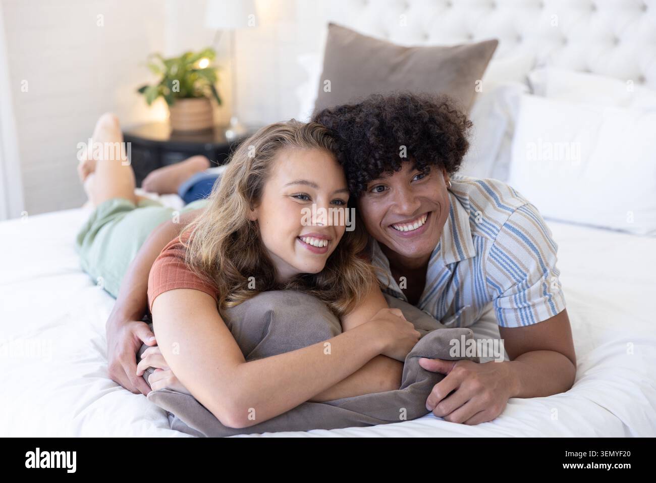 Verschiedene Paare, die sich auf dem Bett in einem hellen Schlafzimmer auf einem weichen grauen Kissen ruhen Stockfoto