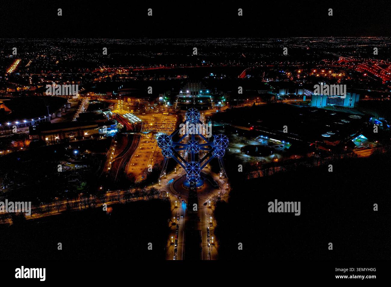 Luftdrohne Nachtsicht auf das beleuchtete Atomium-Denkmal mit blauen LED-Lichtern und Brüsseler Stadtlichtern am Horizont, Laeken, Brüssel, Belgien Stockfoto
