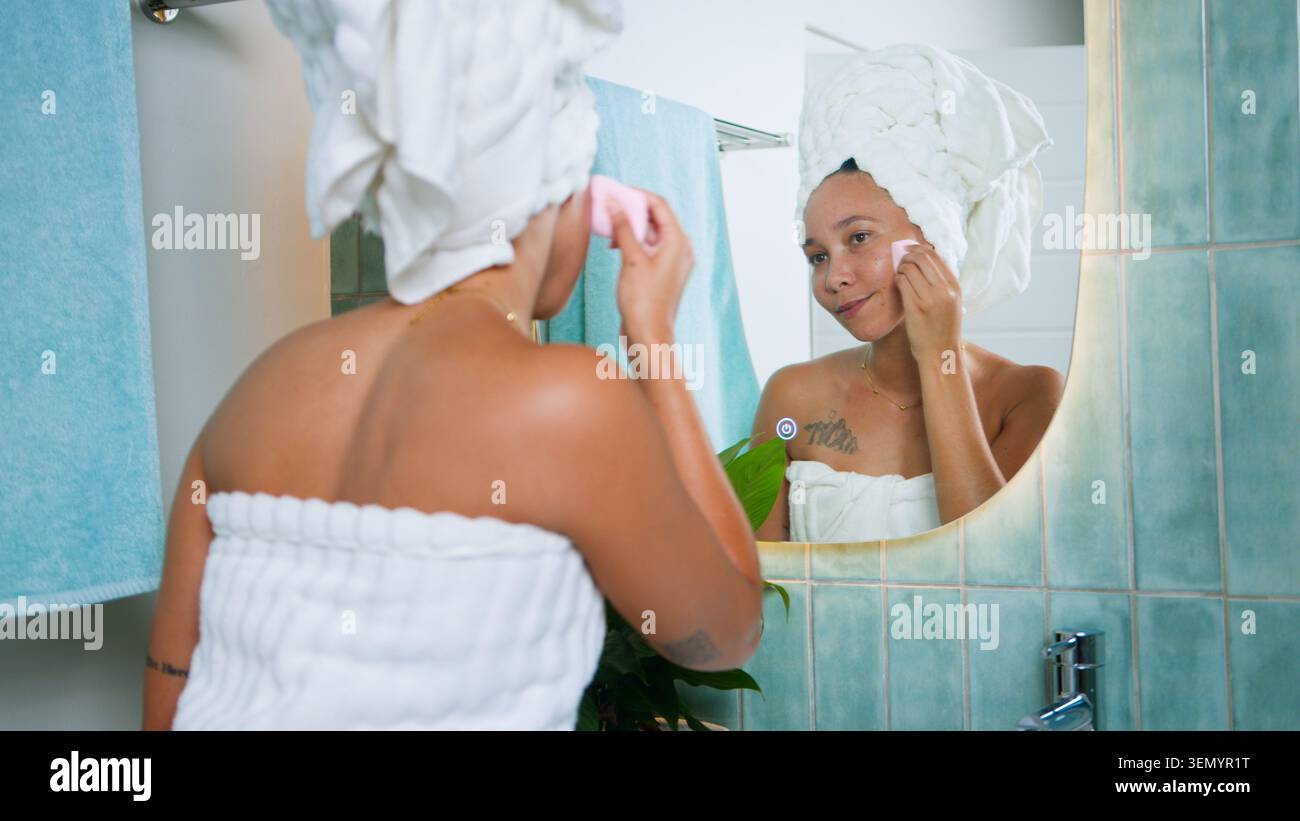 Schwarze Frau, die Hautpflege-Routine im Badezimmerspiegel mit Handtuch Turban und Natural Glow macht Stockfoto