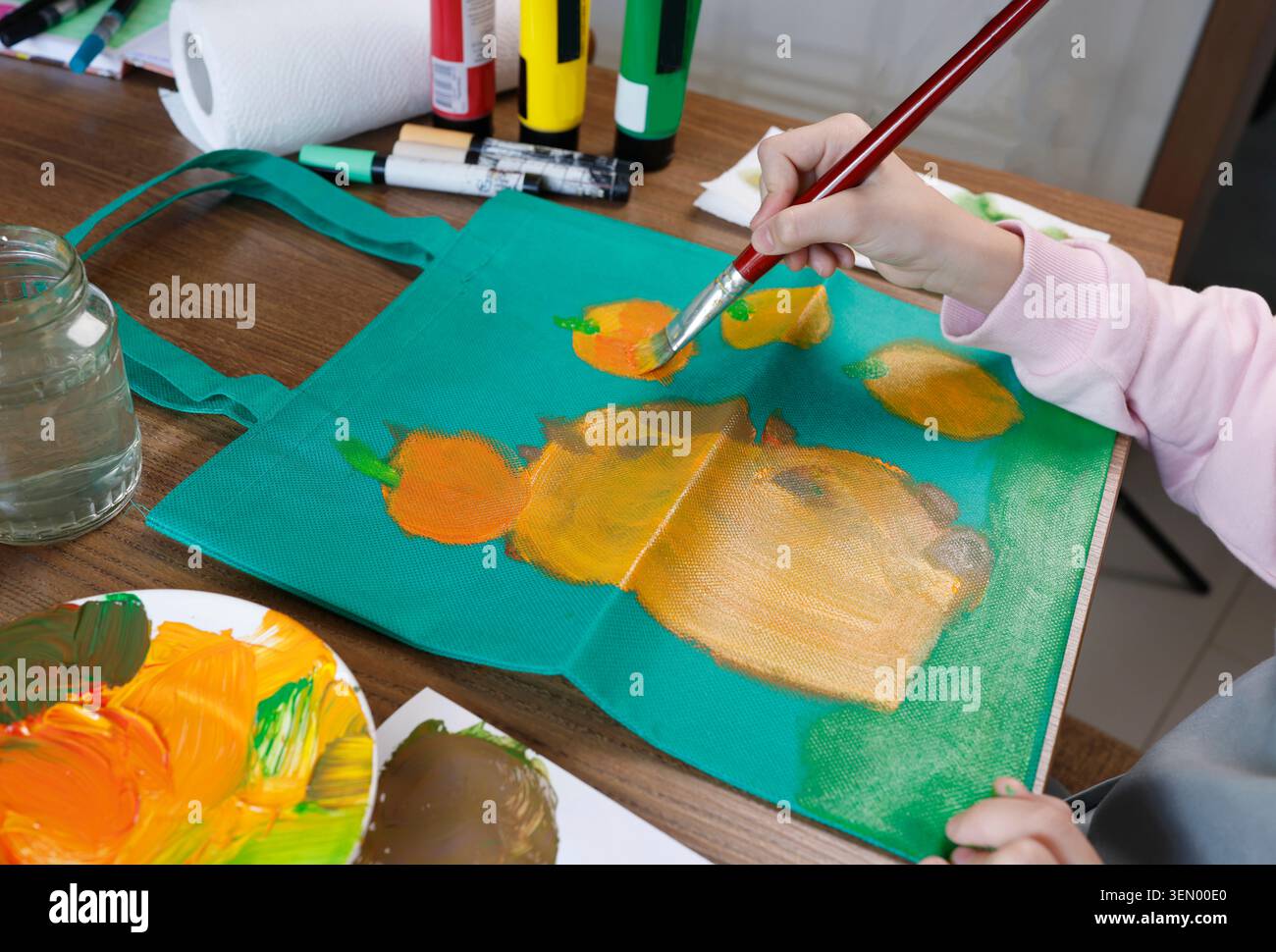 Mädchen im Alter von 11 Jahren malte süße Capybara mit Mandarinen auf grüner Textil-Tragetasche. Kreative handgemachte umweltfreundliche Shopper Dekoration Aktivität für Hobby bei Stockfoto