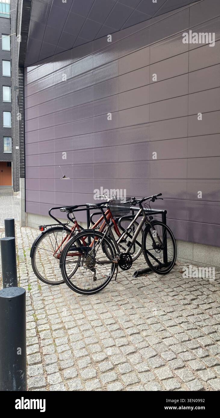 Städtische Fahrräder parken am Fahrradständer neben der Fassade eines modernen Wohngebäudes Stockfoto