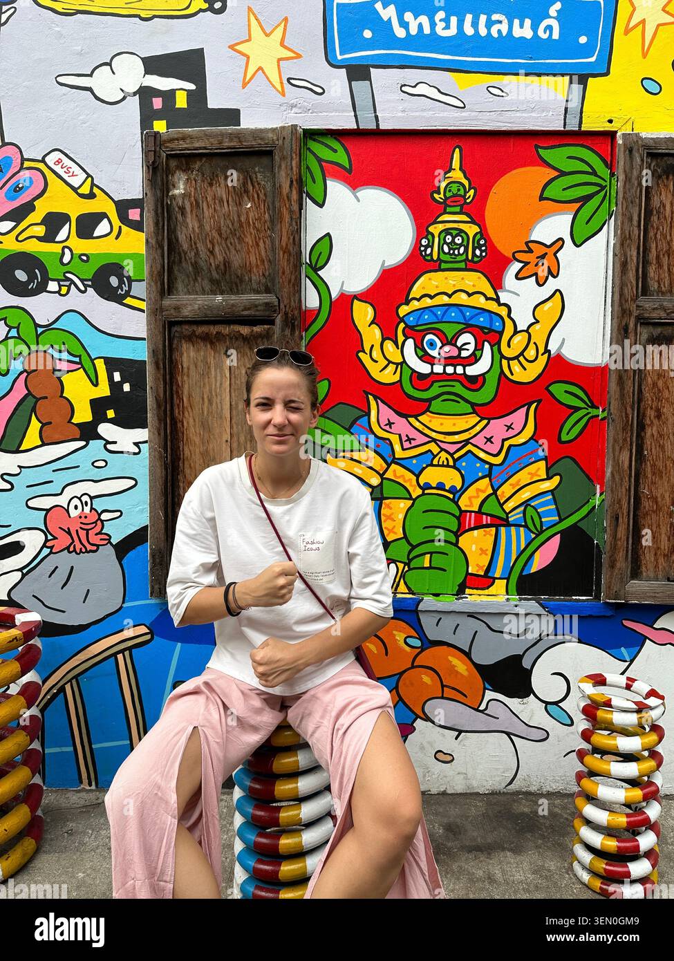 Wall of fame: eine Frau entspannt sich vor einem kühnen thailändischen Riesenmural in Bangkok, Thailand - Smartphone-aufgenommenes Stockfoto