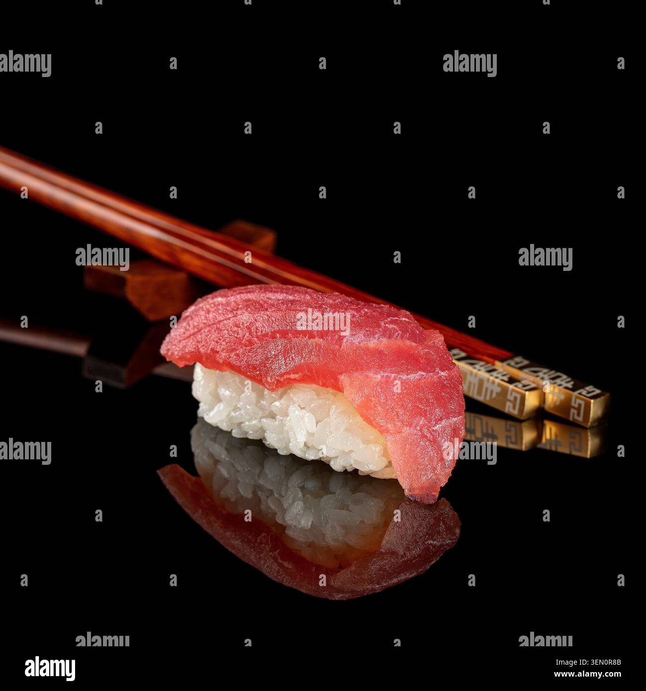 Frisches Thunfisch-Nigiri-Sushi auf glänzend schwarzer reflektierender Oberfläche mit Holzstäbchen und Spiegelreflektion. Stockfoto
