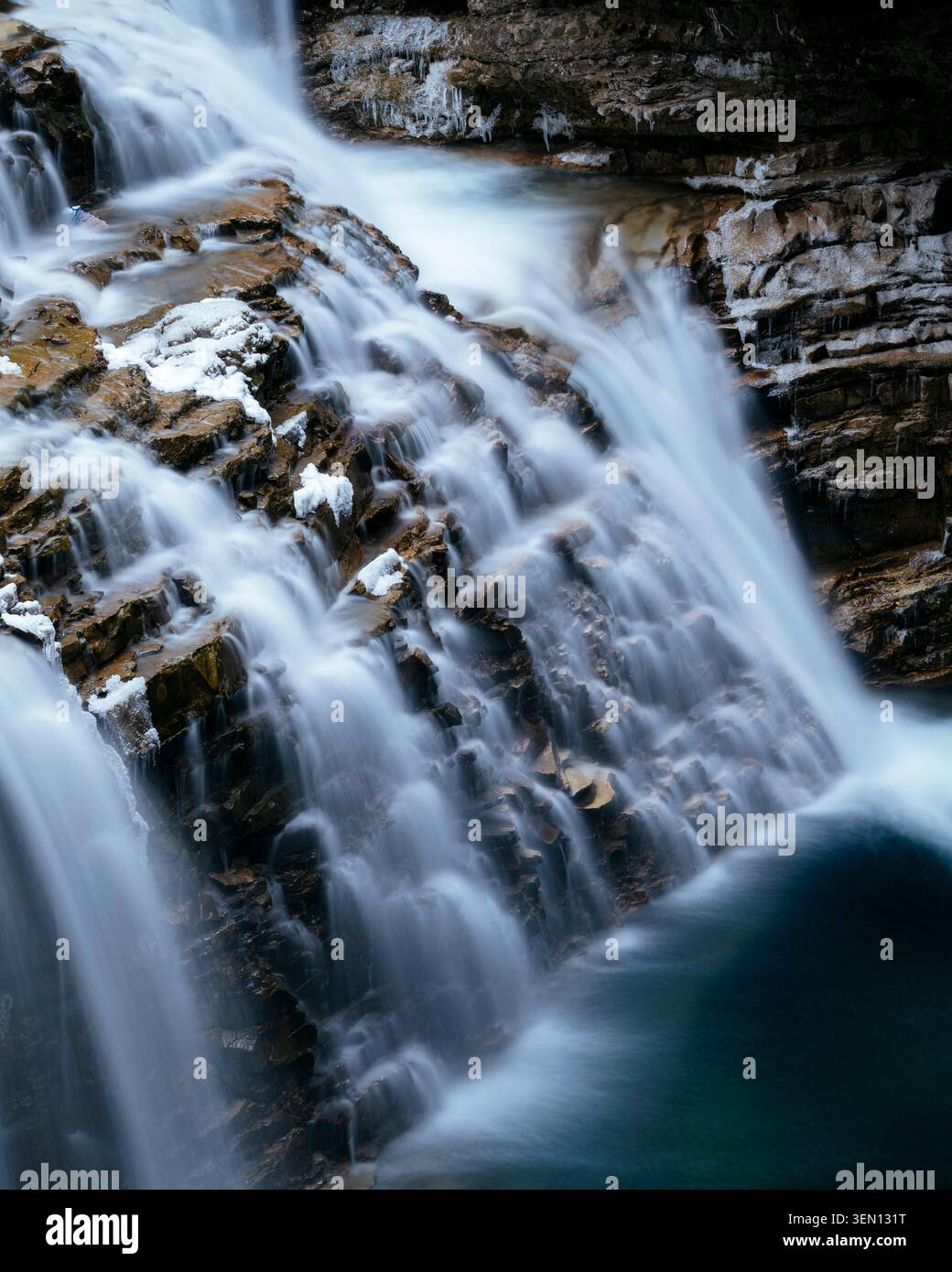 Majestätischer Wasserfall, der über felsige Klippen mit sanft fließendem Wasser und eisigen Details kaskadiert. Stockfoto