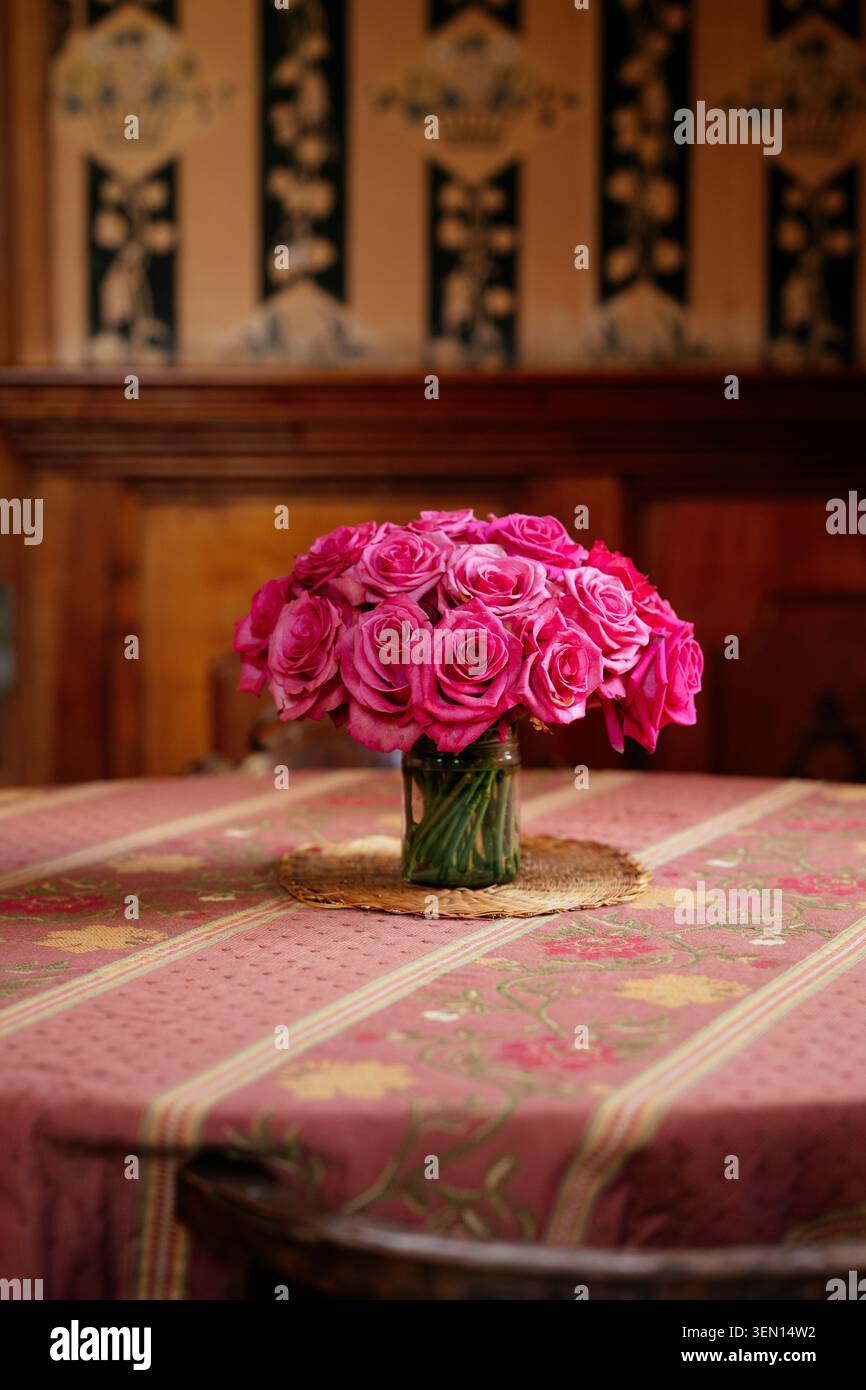 Leuchtend rosa Rosen in einer Vase auf einer gemusterten Tischdecke mit elegantem Hintergrund. Stockfoto