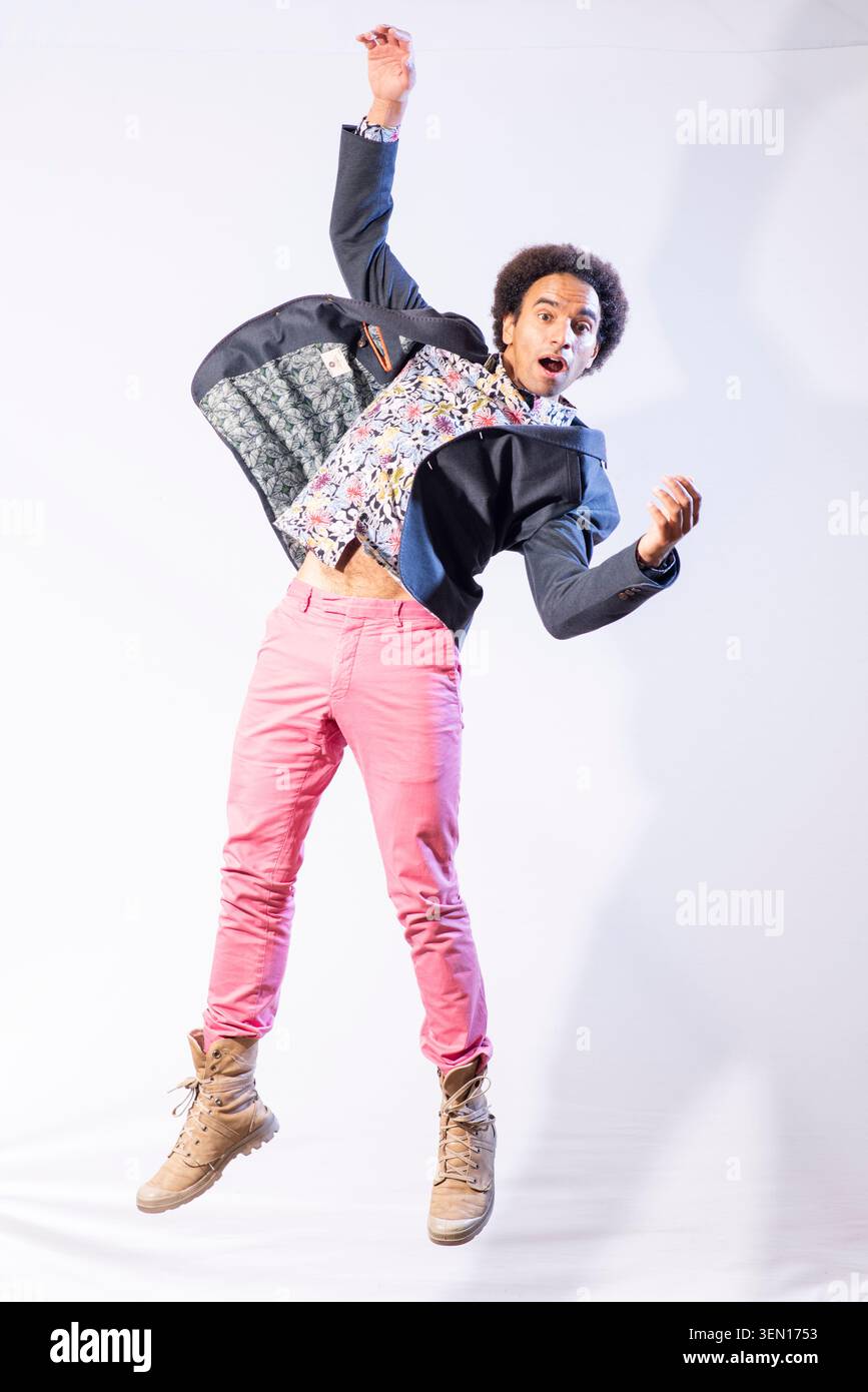 Joseph Coelho macht einen Sprung in einem legeren Outfit mit einem farbenfrohen Hemd und einer pinkfarbenen Hose. Er posiert drinnen und zeigt seinen energiegeladenen Geist. Die Ba Stockfoto