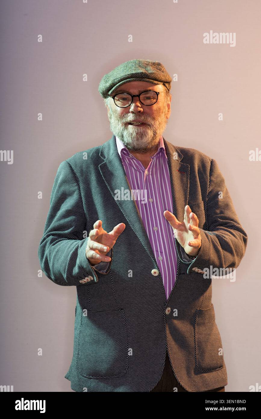 Malachi O'Doherty steht mit erhobenen Händen und lächelt sanft, während er eine Mütze und Jacke trägt. Diese Szene findet während einer öffentlichen Veranstaltung im Jahr 2023 statt Stockfoto