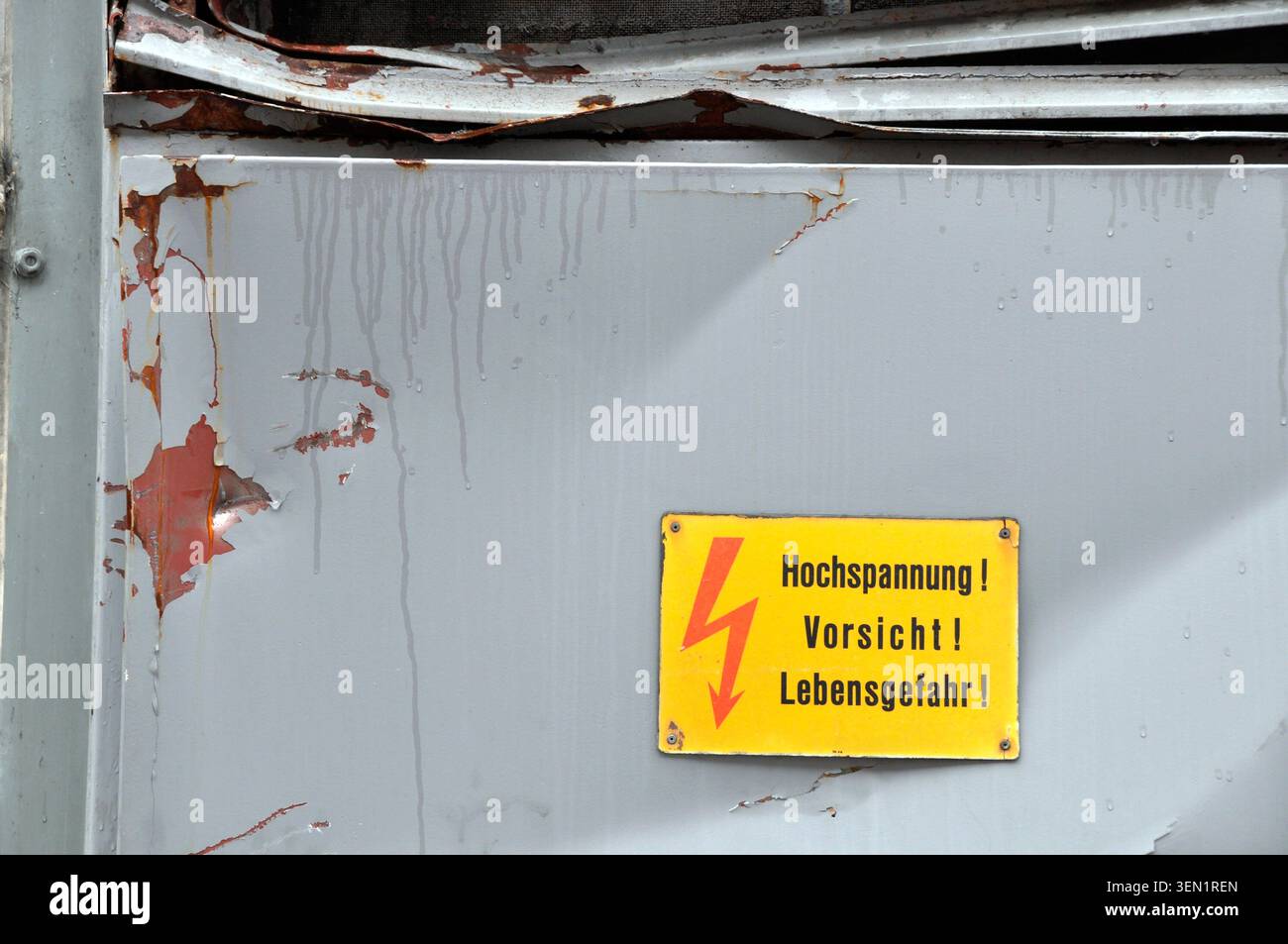 Warnschild: „Vorsicht Hochspannung“ auf abgerissenem grauem Blech Stockfoto