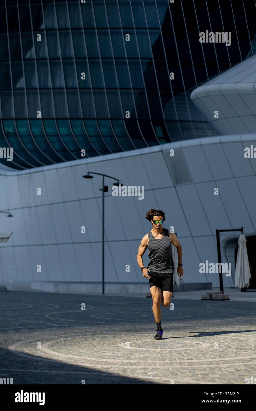 Eine Person in sportlicher Kleidung läuft energisch auf einem Steinweg, der von modernen Gebäuden umgeben ist. Die Szene ist lebendig und voller Leben. Stockfoto