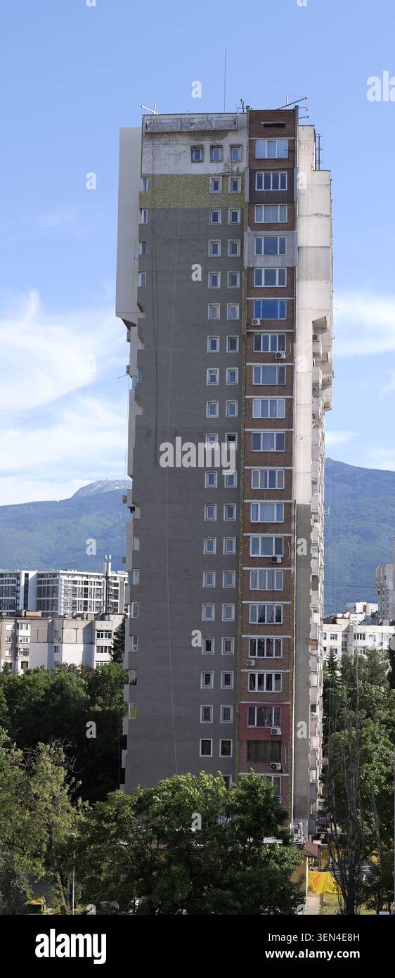 Hoher Wohnblock in sofia, der im Außenbereich renoviert wird, mit Gerüsten und freiliegender Isolierung, im Kontrast zu Alt und Neu, vitosha Berg sichtbar A Stockfoto