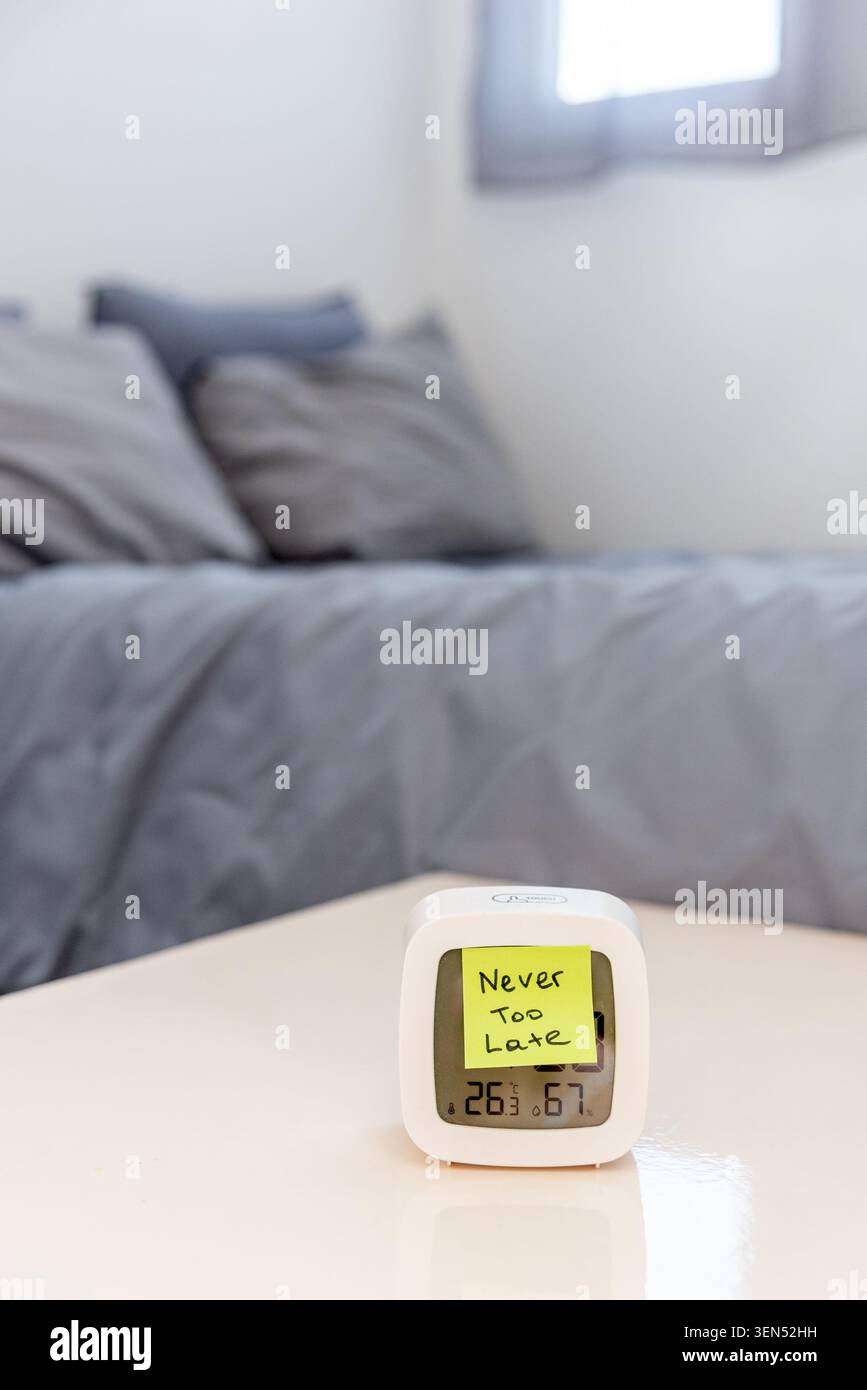 Aufkleber mit Text „Never too Late“ auf dem Wecker im Hintergrund des Schlafzimmers, Motivationshinweis, um die Moral und Neuanfänge zu stärken Stockfoto