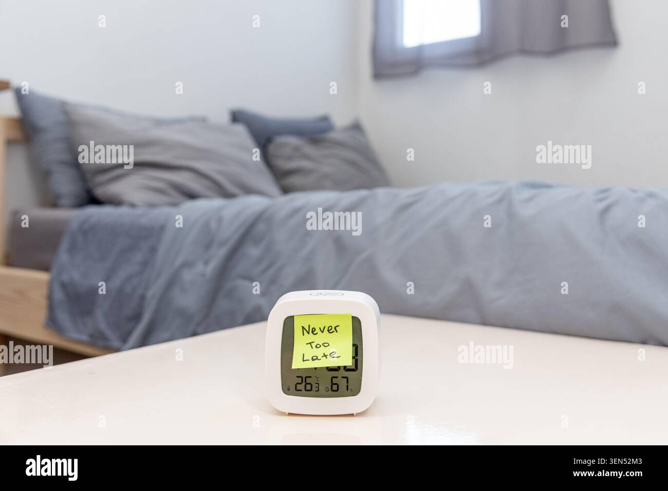 Aufkleber mit Text „Never too Late“ auf dem Wecker im Hintergrund des Schlafzimmers, Motivationshinweis, um die Moral und Neuanfänge zu stärken Stockfoto