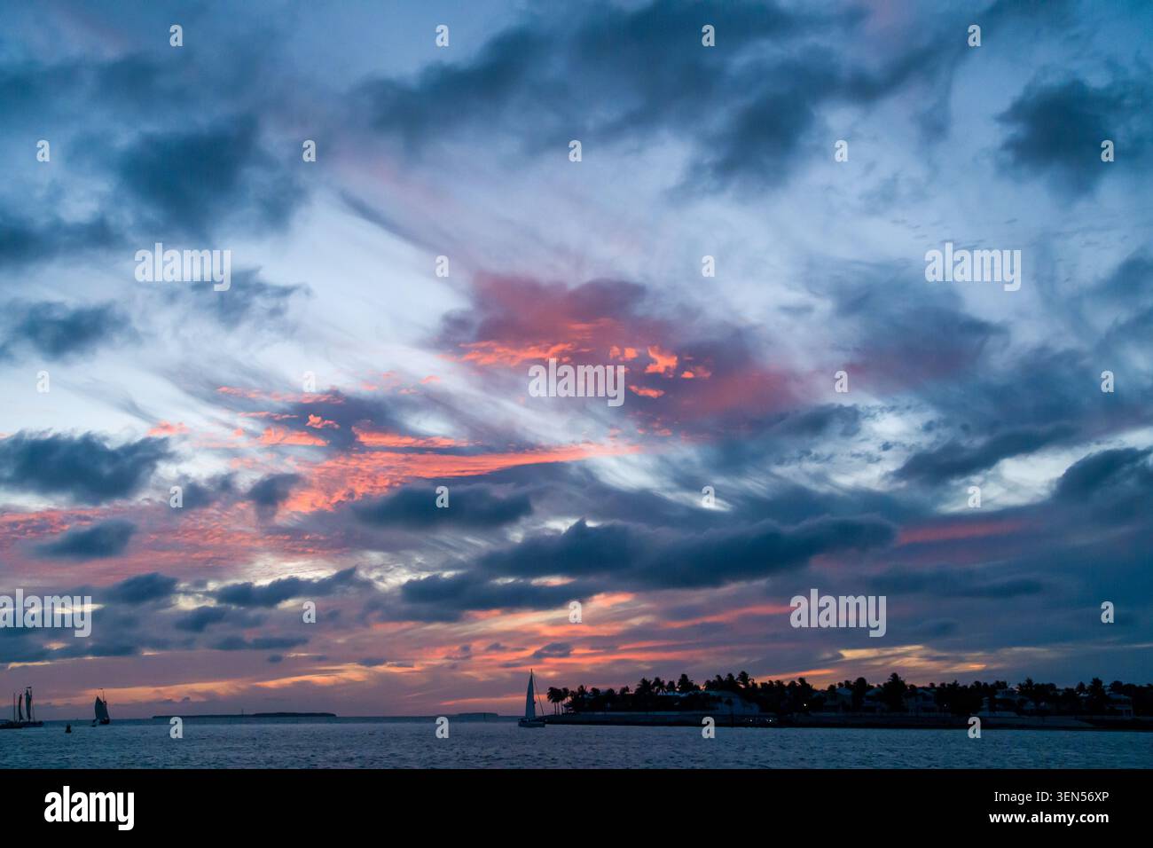 Das kleine Passagiersegelboot überquert den Ozean in der Nähe der dunklen Silhouette von Key West unter einem farbenfrohen Sonnenuntergangshimmel im Sommer. Stockfoto