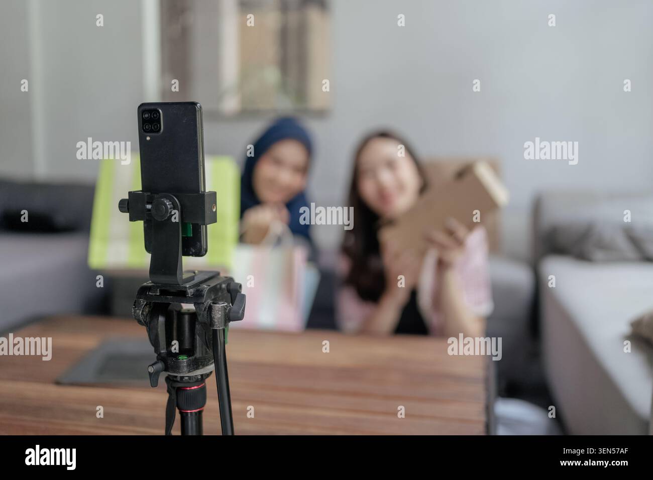 Smartphone auf Stativ mit unscharfen Personen im Wohnzimmer Stockfoto