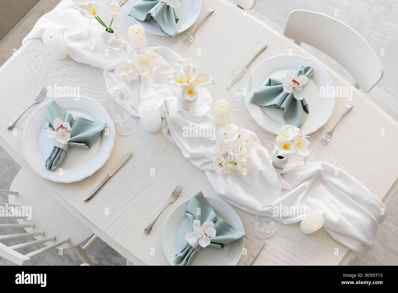 Eleganter weißer Esstisch mit salbeigrünen Servietten, Orchideenakzenten, Kerzen und floralem Herzstück für besondere Anlässe Stockfoto
