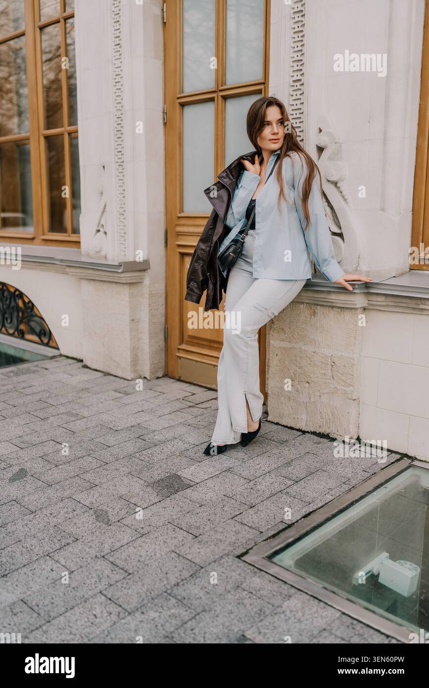 Frau Mode urbane junge Frau mit blauem Hemd und Jeans, die sich an ein klassisches Steingebäude in der Stadt lehnt Stockfoto