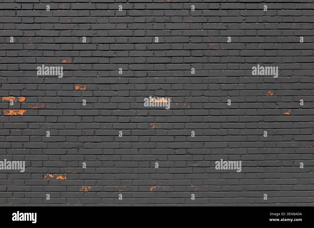 Verwitterte schwarze Ziegelwand mit Flecken, an denen die Farbe abgelöst wurde, wodurch die darunter liegende orange Farbe sichtbar wird. Hintergrund für Kopierraum abschleifen. Stockfoto