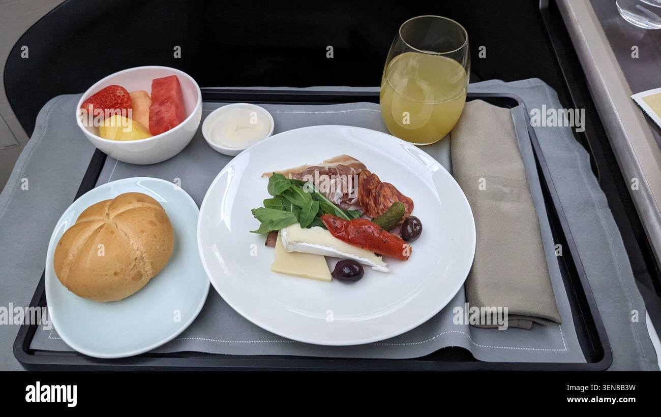 Elegantes Essen der Business Class mit frischem Obst, Gourmet-Käseplatte, Schinken und Orangensaft auf einem Tablett. Stockfoto