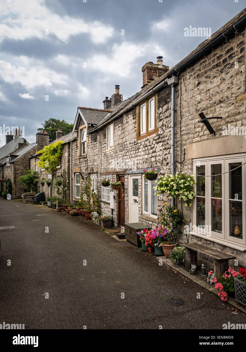 Linearer Blick auf die Straße mit Blick auf eine Reihe traditioneller Steinhäuser, die mit Sommerblumen geschmückt sind, auf dem Fountain Square im Dorf Tideswell Stockfoto