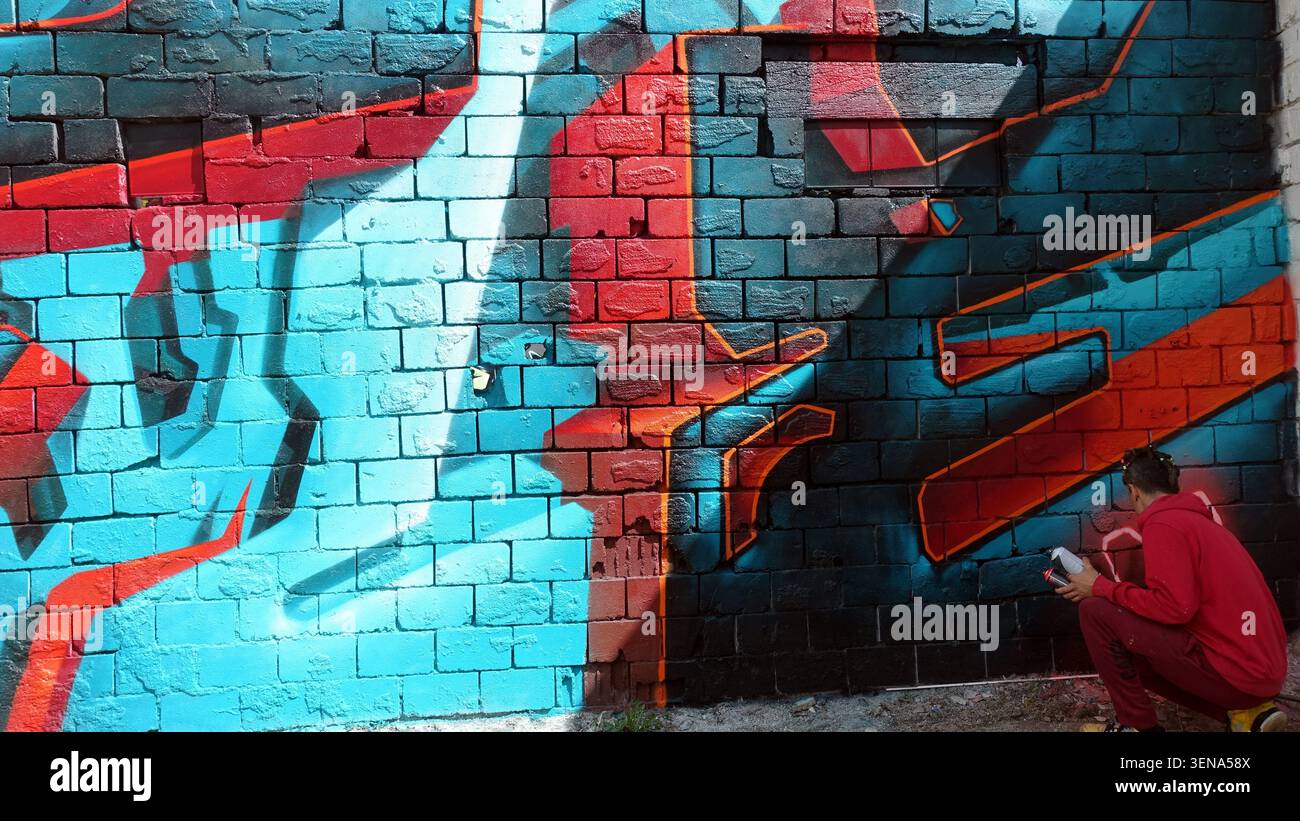 Stockholm, Schweden, 17. Mai 2026. Ein Straßenkünstler malt ein leuchtendes blau-rotes Graffiti-Wandgemälde auf einer strukturierten Ziegelwand, das urbane Kreativität zum Ausdruck bringt, b Stockfoto