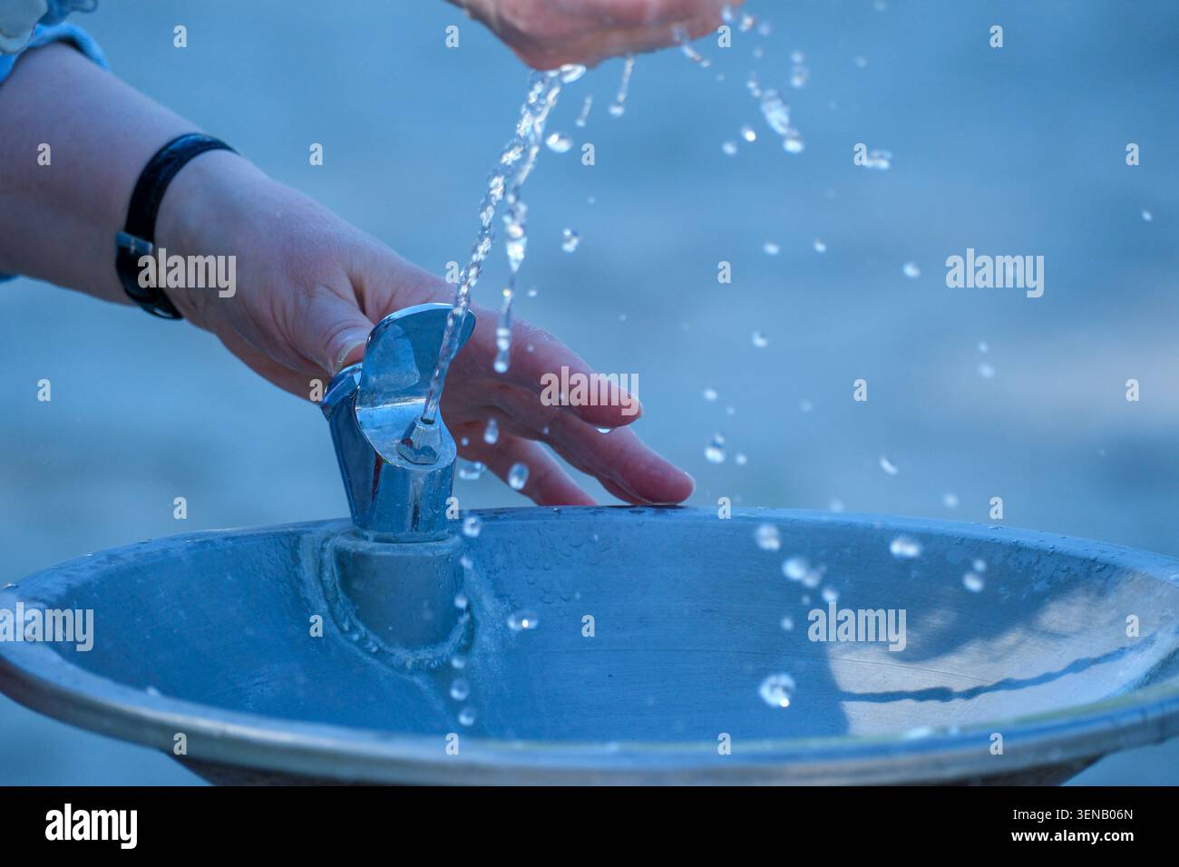 Eine Hand berührt anmutig das kühle Wasser eines Springbrunnens unter hellem Sonnenlicht. Stockfoto