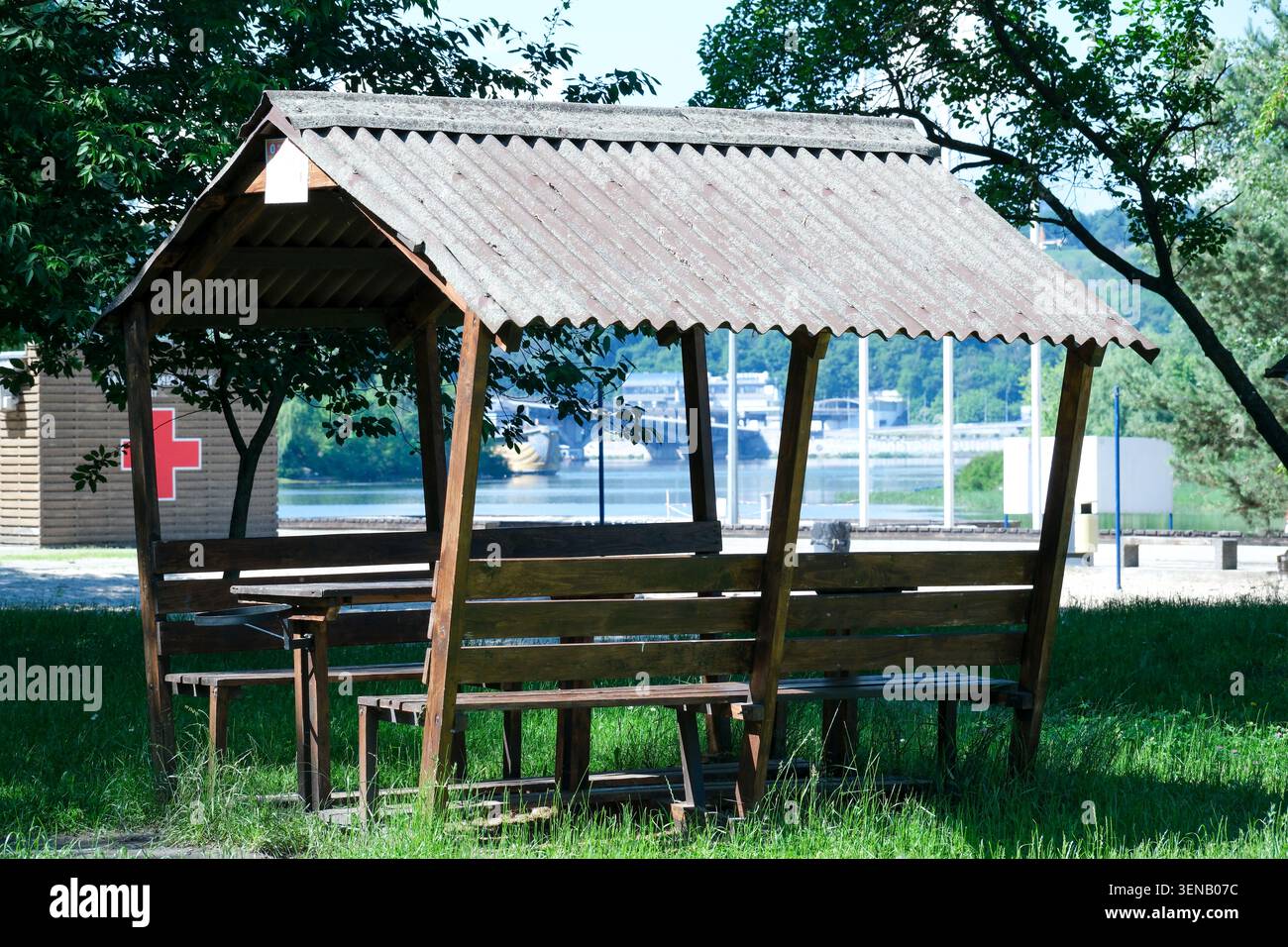 Ein charmanter Holzunterstand bietet Schatten am Fluss, umgeben von üppigem Grün. Stockfoto