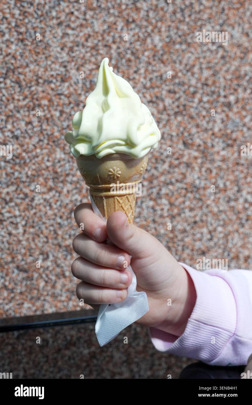Die Hand eines Kindes, die eine Eiskugel auf einem Steingrund hält Stockfoto