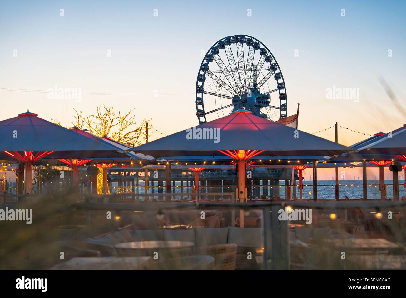 Strandresort Scheveningen bei Sonnenuntergang mit Riesenrad, Sonnenschirmen und Küstenpromenade im H Stockfoto