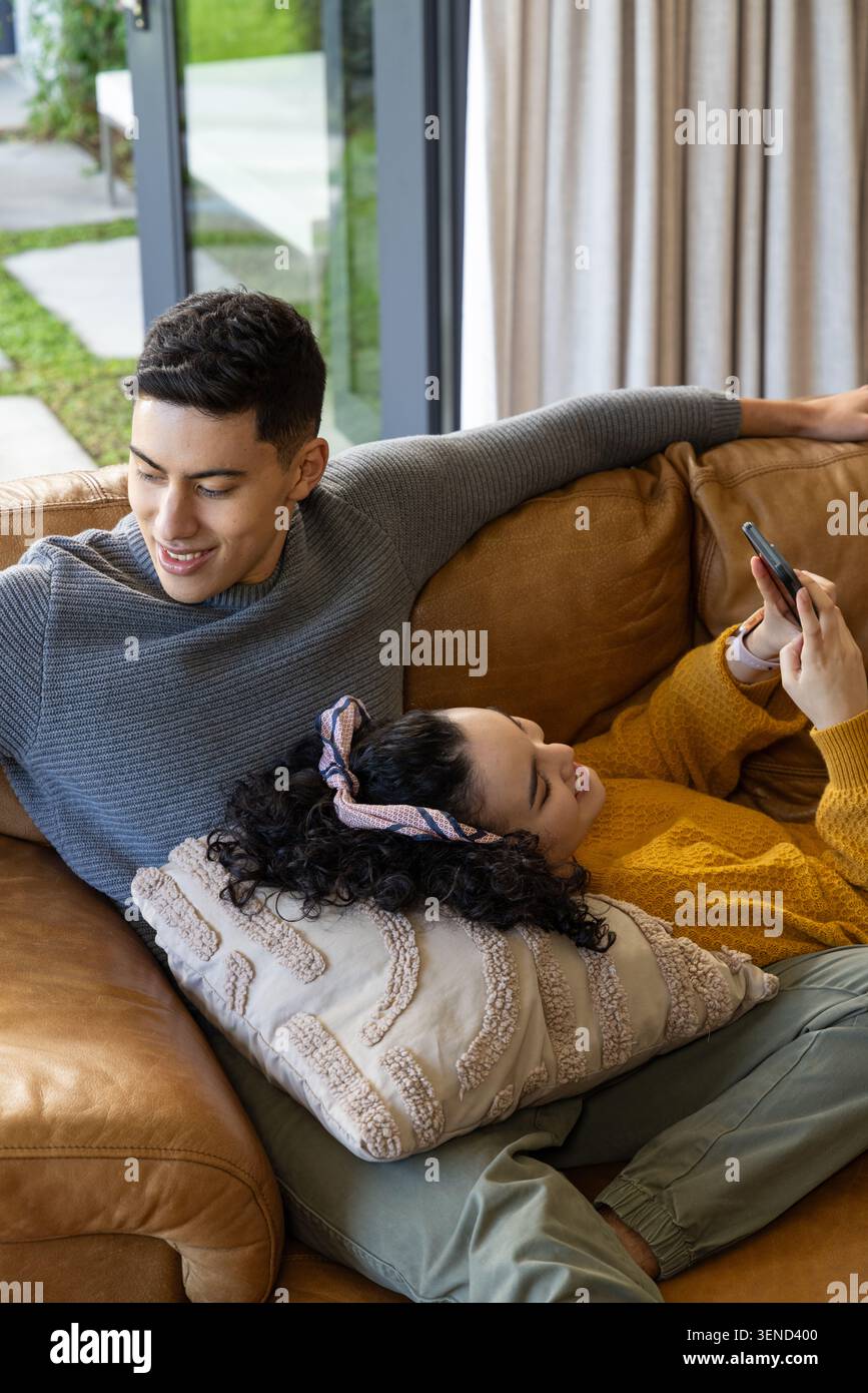 Paare sitzen auf braunem Ledersofa von Glastür Mann in grauem Pullover, Frau mit Smartphone Stockfoto