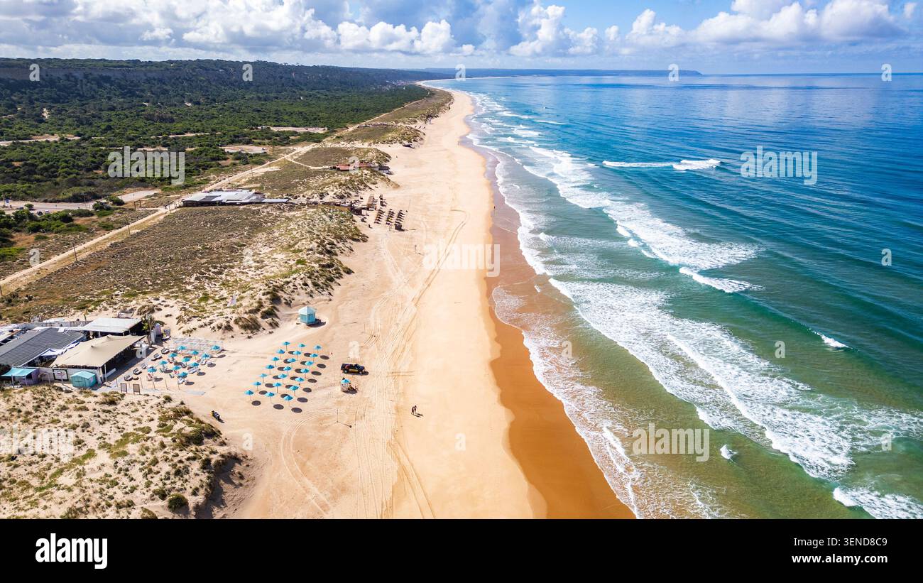 Costa Caparica, Lissabon. Blick aus der Vogelperspektive auf den Strand Costa Caparica, Portugal, mit goldenem Sand, türkisfarbenem Wasser und sanften Wellen. Üppige grüne Linien t Stockfoto