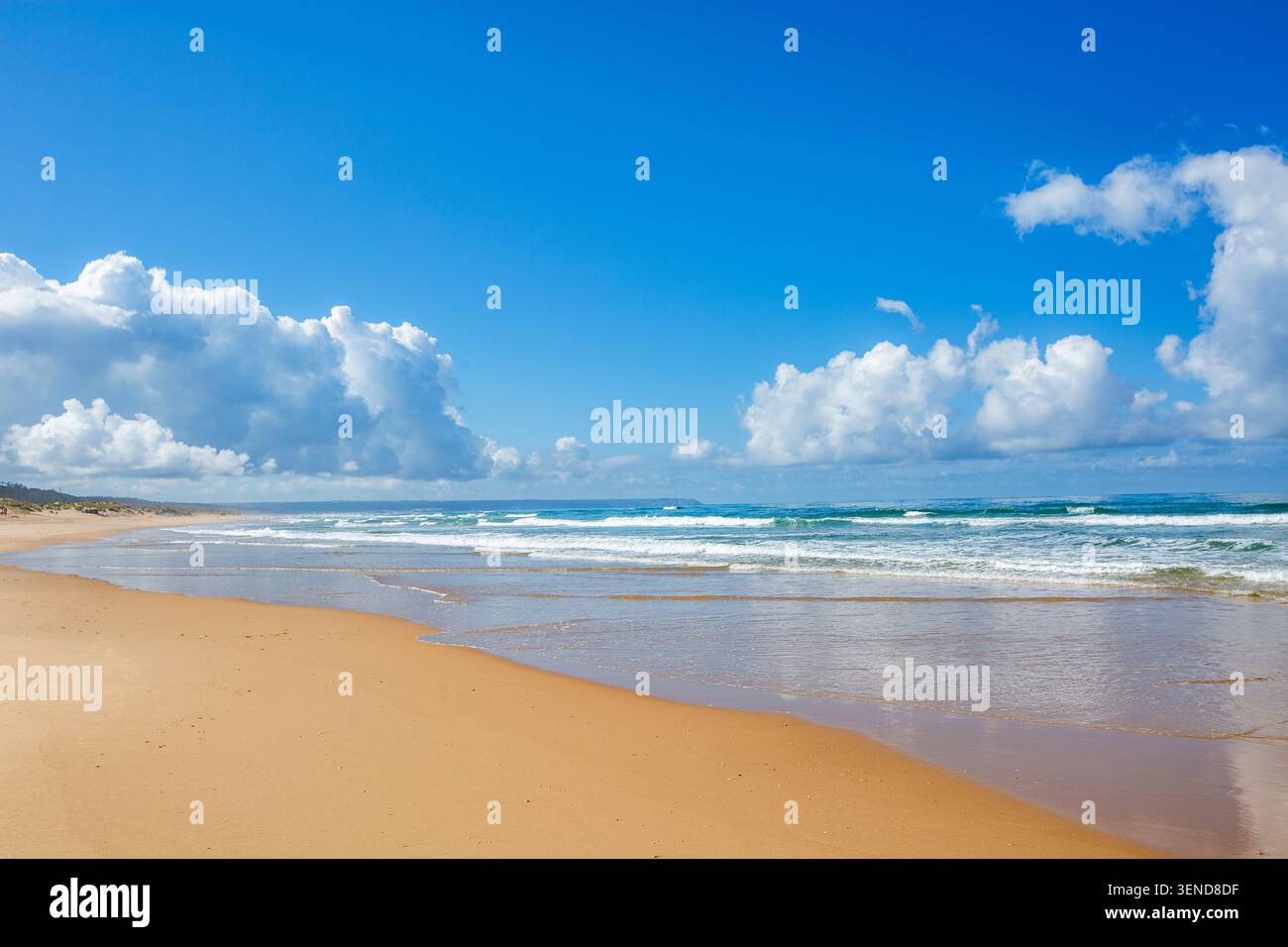 Costa Caparica, Lissabon. Wunderschöne Strandszene mit goldenem Sand und blauen Meereswellen. Hellblauer Himmel mit flauschigen weißen Wolken. Wasserfunkel Stockfoto