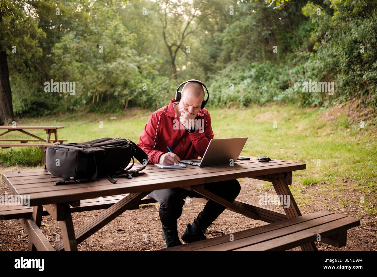 Mann, der sich während der Arbeit im Park auf sein Notebook und seinen Laptop konzentriert Stockfoto