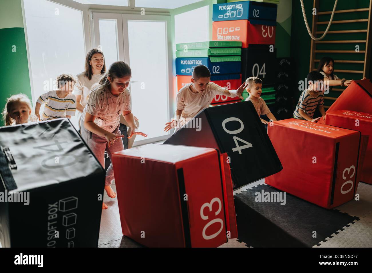 Kinder spielen einen Indoor-Hinderniskurs in einem Fitnessstudio mit weichen Plyboxen und Lehrer Stockfoto