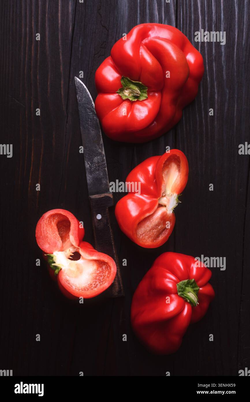 Rote Paprika mit geschnittenen Stücken auf dunklem Hintergrund. Frischer süßer Pfeffer, gesunde Kochzutat Stockfoto